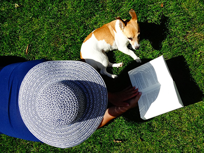 Sunbathing with a dog, book and wearing a sunhat, top view